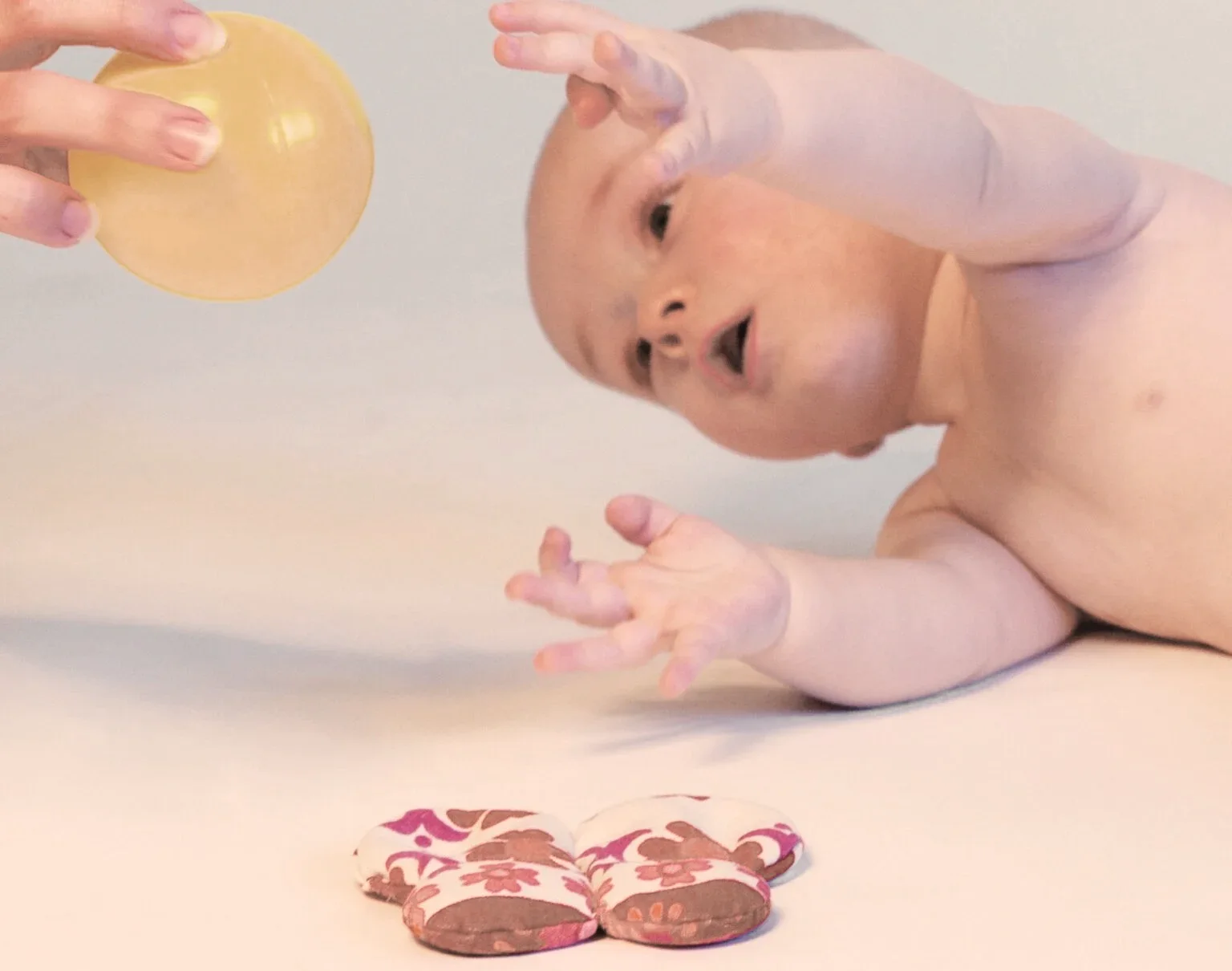 Baby in Bauchlage streckt sich nach einem gelben Ball